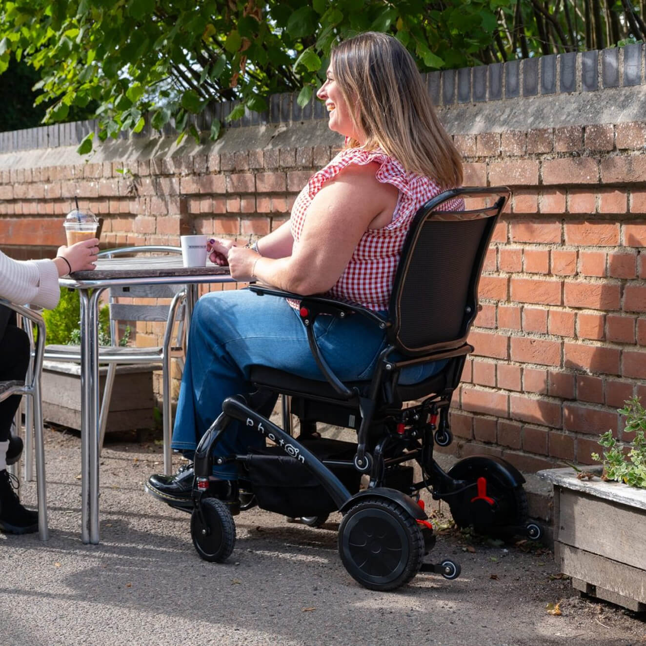 A woman having a coffee with a friend, on Photon powerchair